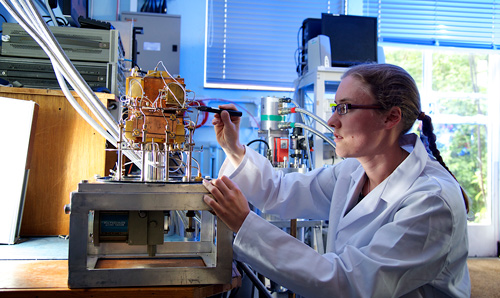 A female fellowship researcher in a white lab coat adjusting wires on a machine