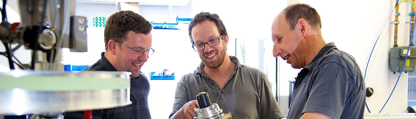 Three researchers inspecting cryostat equipment