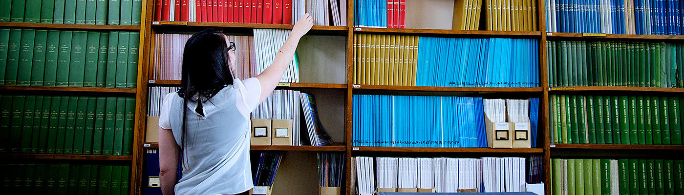 A researcher reaching up to books in a colourful library