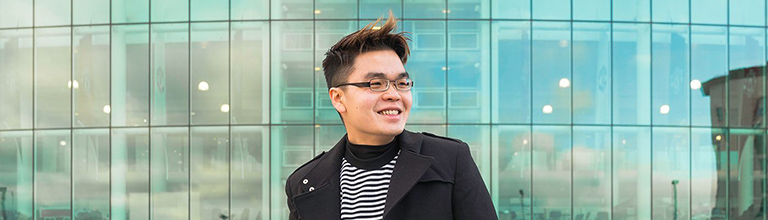 Male student smiling in front of Old Trafford's exterior