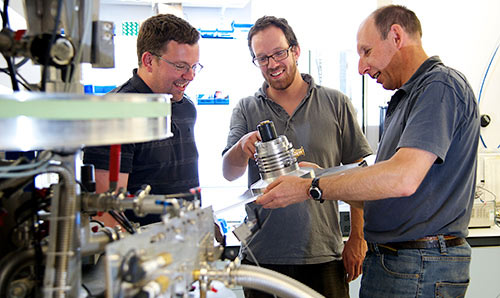 Three researchers examining equipment in a cryostat laboratory