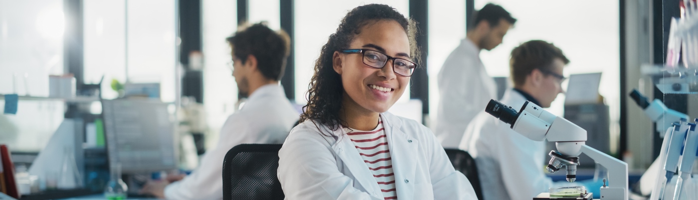 Student scientist smiling to camera next to a microscope 